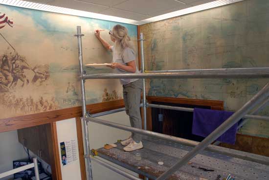 Artist at work restoring veterans memorial mural at North Clinic Building.